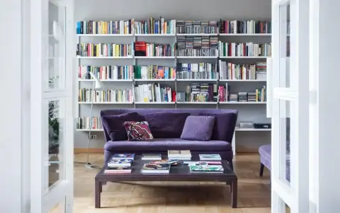 Un divano viola accogliente davanti a una libreria bassa piena di libri e CD.