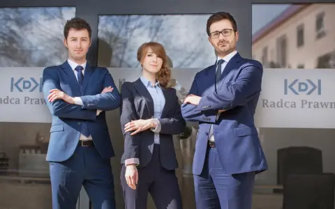 Trzech prawników w garniturach stoi przed budynkiem z logo "Radca Prawny".