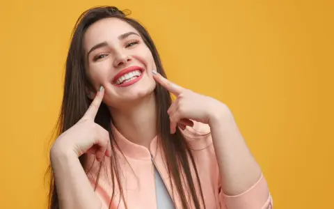 Une jeune femme au sourire éclatant, doigts pointés vers ses joues, semble expliquer la signification d'un sourire pincé.