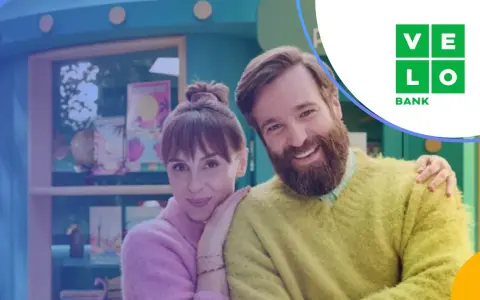Uśmiechnięta para przed budką z logo Velo Bank. Dowiedz się, velo bank co to za bank i jakie ma oferty.