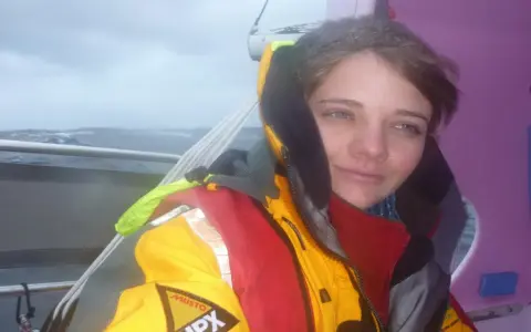 Dziewczyna która opłynęła świat, w sztormowym morzu, w jaskrawej kurtce żeglarskiej, z determinacją w oczach.