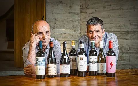 Dos hombres sonríen detrás de una fila de botellas de vino. Uno de ellos es el dueño de Bodegas Olarra.