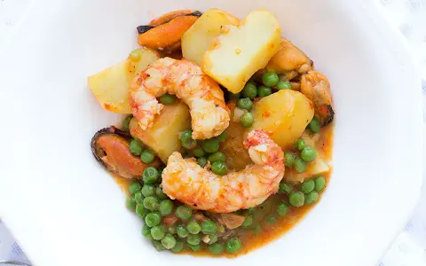 Patatas a la marinera con gambas, mejillones y guisantes en una salsa sabrosa.