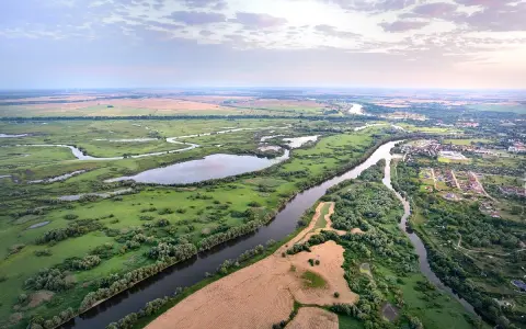 Malownicza dolina rzeki Odry z licznymi meandrami, zielonymi łąkami, polami i niewielką wsią po prawej stronie.