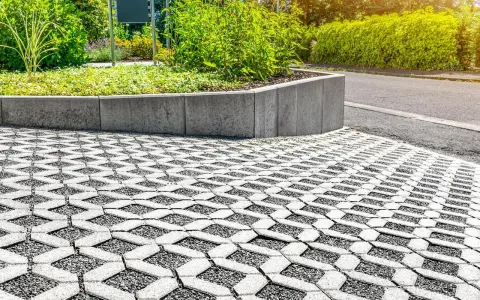 Przestrzeń z ażurową nawierzchnią, która zapewnia minimalną powierzchnię biologicznie czynną, otoczona zielenią i betonowym murkiem.