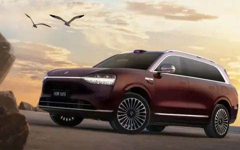 Ciemnoczerwony SUV Aito M9 na tle zachodzącego słońca, z ptakami w locie.