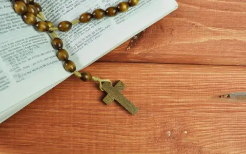 Różaniec na drewnianym stole obok Biblii, przypominający o 10 przykazaniach kościelnych i modlitwie.
