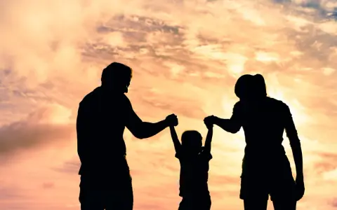 Siluetas de una familia jugando bajo un cielo anaranjado. Un niño es levantado por sus padres, un ejemplo de aprendizaje social y emocional.
