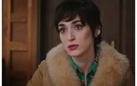 Una donna con un taglio di capelli corto e scuro, trucco marcato e un cappotto di pelliccia chiara. Le anticipazioni di Cuori 3 promettono colpi di scena.