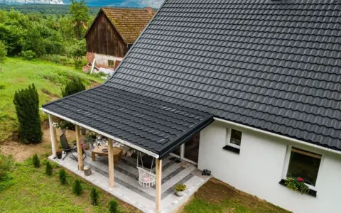 Nowy, czarny dach z blachodachówki nad tarasem i domem. Wymiana dachu zakończona sukcesem, dom zyskał nowy, nowoczesny wygląd.