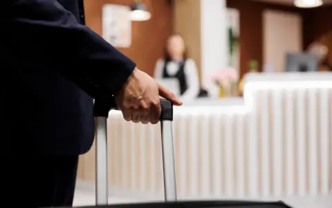 Mężczyzna w garniturze trzyma walizkę, zbliżając się do recepcji hotelowej. Czas na depozyt w hotelu i nowy początek podróży.