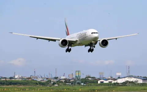 Emirates Boeing 777 zbliża się do lądowania. W tle widać przemysłowy krajobraz i inne samoloty na niebie, sugerujące ruch lotniczy, być może związane z dżerba loty.