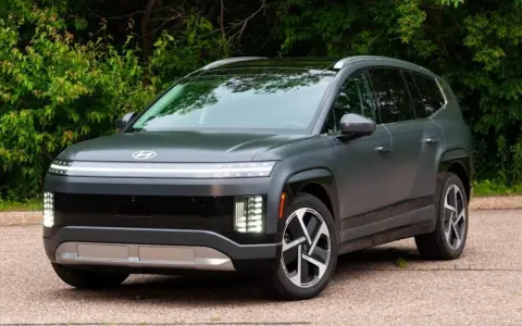 Szary SUV Hyundai IONIQ 9 z charakterystycznym pasem świateł z przodu, na tle zieleni.