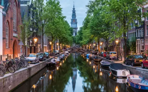 Kanał w Amsterdamie z łodziami, rowerami i wieżą kościelną w tle.