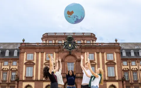 Studierende werfen einen Globus in die Luft vor dem Gebäude des akademischen Auslandsamtes.