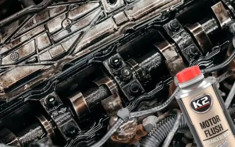 Silnik Peugeot 307 1.6 benzyna po płukaniu. Widać wałki rozrządu i elementy pokryte olejem. Obok butelka płukanki K2 Motor Flush.