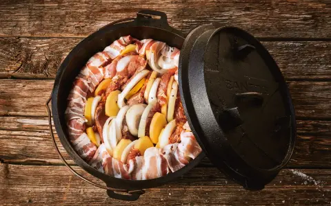 Dutch oven mit Fleisch, Kartoffeln und Zwiebeln, bereit für köstliche Dutch Oven Rezepte auf dem Gasgrill.