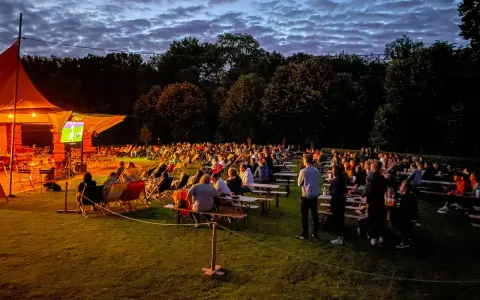 Menschen genießen ein Fußballspiel beim Public Viewing in Berlin unter einem dramatischen Abendhimmel.