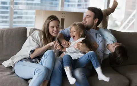 Eine Familie lacht und spielt auf dem Sofa. Das gemeinsame Lachen ist ein schönes Ritual.