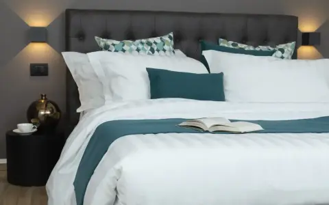 Letto rifatto con lenzuola bianche e copriletto turchese. Un libro aperto è posato al centro, pronto per essere letto. Ecco come si mette il lenzuolo di sopra.