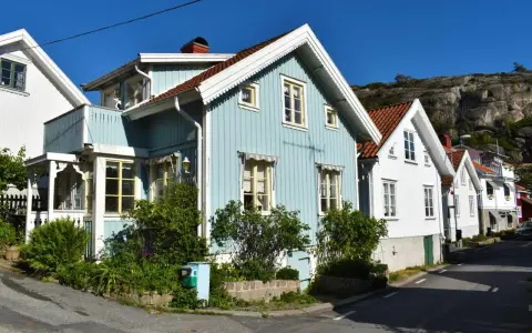 Blå och vita trähus längs en gata, med klippor i bakgrunden. Undrar hur mycket fastighetsskatt dessa vackra hus har.