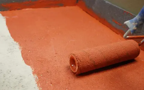 Rodillo aplicando imprimación roja en el suelo de un garaje. La superficie está parcialmente cubierta, mostrando el antes y el después.