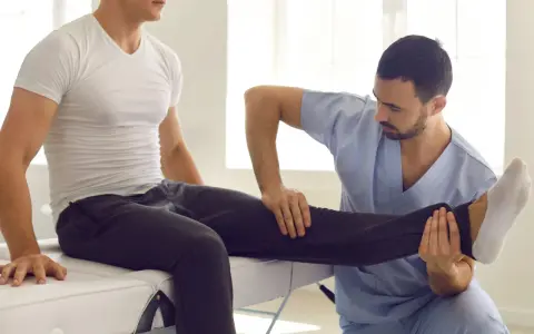 Fizjoterapeuta wykonuje zabiegi rehabilitacyjne, delikatnie unosząc nogę pacjenta.
