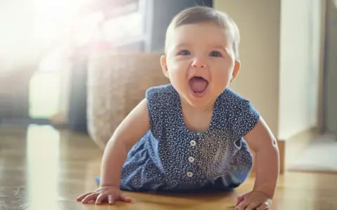 Ein fröhliches Baby hebt Arme und Beine in Bauchlage, bereit zum Krabbeln.