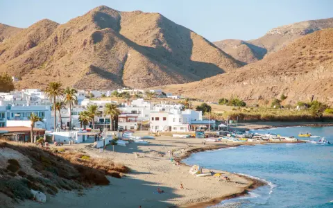 Pueblos de Almería con playa, casas blancas y palmeras junto a un mar azul, con montañas áridas de fondo.