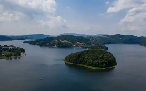 Widok z lotu ptaka na jezioro z wyspą porośniętą lasem i otoczone wzgórzami.