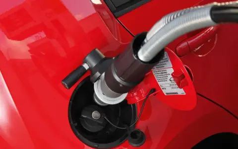 Tankowanie auta gazem CNG. Wlew paliwa w czerwonym samochodzie, do którego podłączona jest dysza.