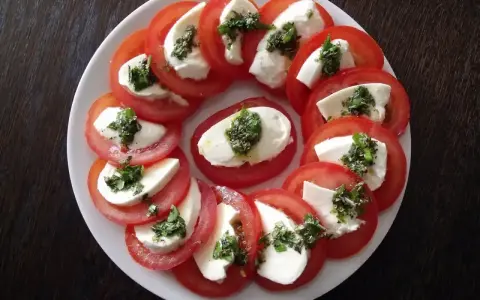 Pyszne pomidory z mozzarellą, ułożone na talerzu, ozdobione ziołami. Idealna przekąska na lato.