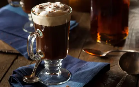 En värmande irish coffee med vispad grädde och kanel på en blå duk.
