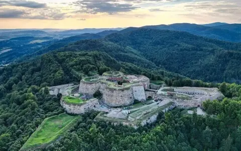 Twierdza na wzgórzu, niczym srebrna góra, otoczona zielonymi lasami.
