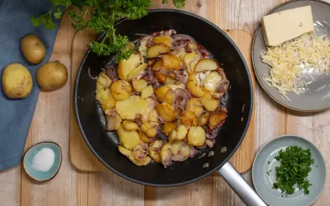 Bratkartoffeln rezept: goldbraune Kartoffeln mit Zwiebeln und Käse in der Pfanne, dazu frische Petersilie und Salz.