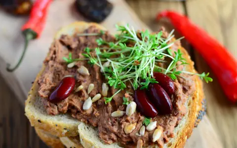 Pyszna pasta z czerwonej fasoli na chlebie, ozdobiona kiełkami i nasionami. Obok leżą czerwone papryczki chili.