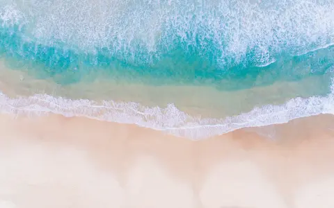 Vue aérienne d'une photo à la plage, avec des vagues turquoise déferlant sur le sable doré.