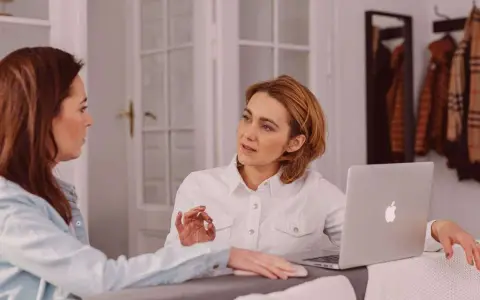 Dos mujeres discuten un traspaso de negocio en funcionamiento. Una tiene un portátil abierto.