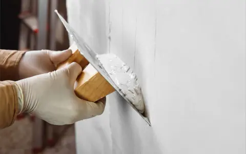 Manos enguantadas aplican yeso a una pared con una llana. La pregunta es: cuanto tarda en secar el yeso.