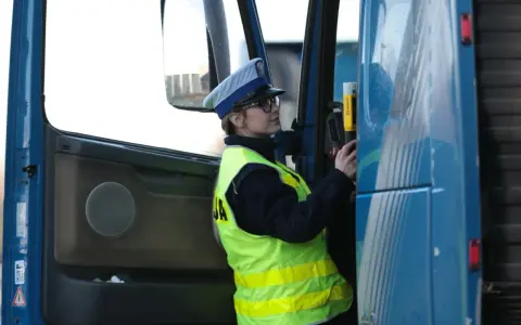 Policjantka w kamizelce odblaskowej i czapce przykłada alkomat do drzwi ciężarówki.