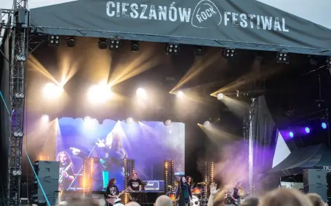 Zespół gra na scenie podczas Cieszanów Rock Festiwal. W tle wielki ekran z wizerunkiem wokalistki i reflektory.