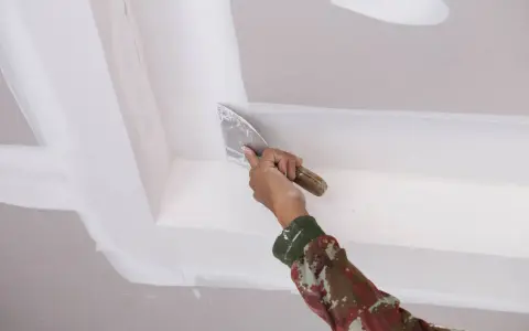 Mano con espátula aplica masilla para pegar escayola rota en el techo.