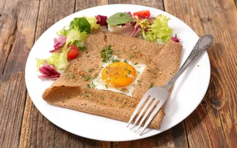 Galette bretonne complète au four, garnie d'un œuf au plat, d'herbes et servie avec une salade fraîche.