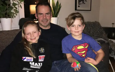 Marcus Oscarsson med sin familj, dottern och sonen sitter glatt i soffan.