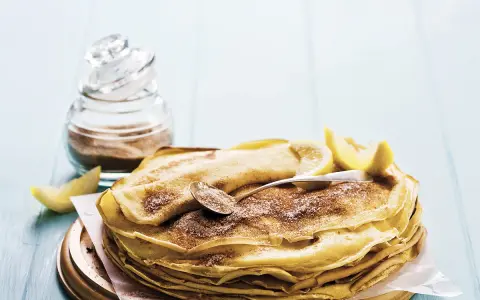 Pile de crêpes au lait entier, saupoudrées de sucre et de cannelle, garnies de quartiers de citron. Un délice simple et gourmand.