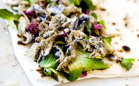 Sardoncini al testo su piadina con insalata fresca e cipolla rossa. Un sapore di mare e terra.