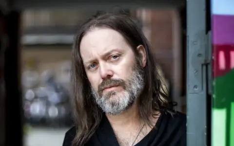 Niclas Frisk med långt hår och skägg, blickar mot kameran.