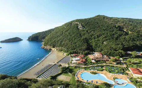 Villaggio toscana sul mare con spiaggia attrezzata, piscine e rigogliosa vegetazione che abbraccia la costa.