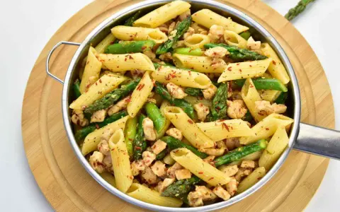 Penne z kurczakiem i szparagami, posypane płatkami chili. Pyszne danie na szybki obiad.