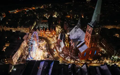 Lichterglanz auf dem Weihnachtsmarkt Schleswig-Holstein: Ein Riesenrad dreht sich neben einer Kirche, während Schneeflocken fallen.